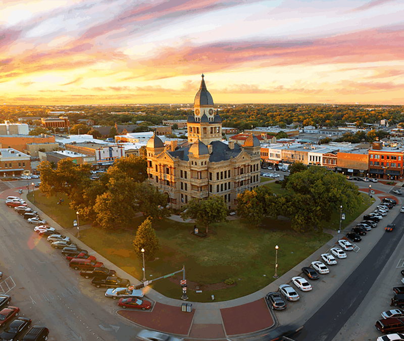 Historic Denton County Courthouse at sunset, surrounded by trees and downtown buildings, showcasing the vibrant community of Denton, TX.